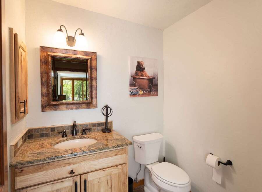 This charming bathroom features a rustic wooden vanity with a granite countertop and a tiled backsplash, complemented by a decorative mirror and a whimsical bear-themed artwork.