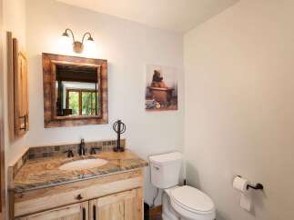 This charming bathroom features a rustic wooden vanity with a granite countertop and a tiled backsplash, complemented by a decorative mirror and a whimsical bear-themed artwork.