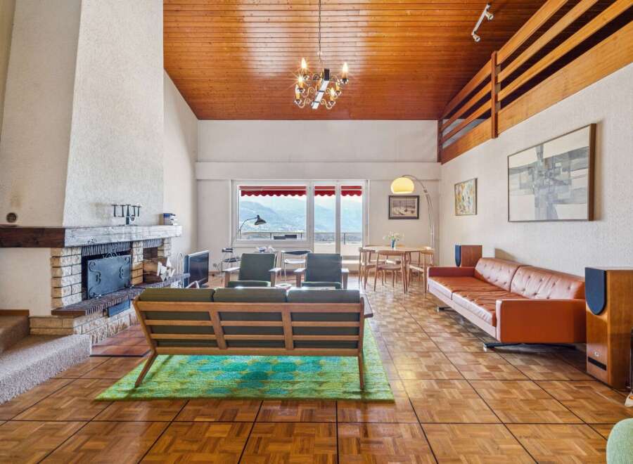 Experience breathtaking mountain views from this stunning living room, featuring a cozy fireplace and a vaulted wood-paneled ceiling.