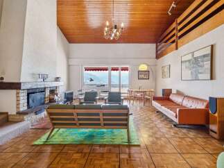 Experience breathtaking mountain views from this stunning living room, featuring a cozy fireplace and a vaulted wood-paneled ceiling.