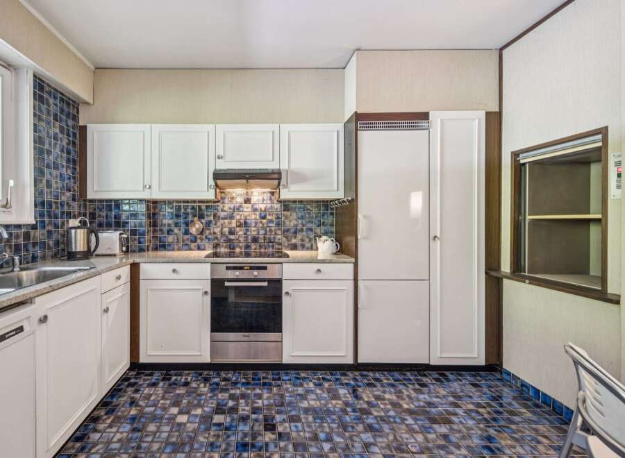 This charming kitchen features a unique blue and brown tiled backsplash and matching floor, creating a retro yet stylish aesthetic.