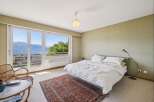 Experience breathtaking panoramic views from this serene bedroom, featuring a large window overlooking a stunning lake and mountains.