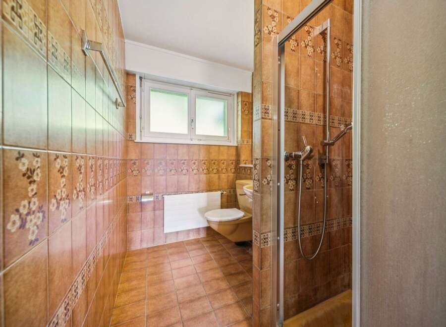 This bathroom features warm, earthy tones with decorative floral tiles and a complementary tiled floor.