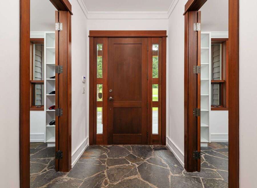 Step into a grand entryway featuring a rich, dark wood door with elegant glass panels, inviting natural light into the home.