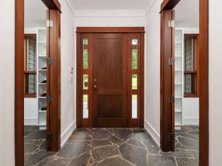 Step into a grand entryway featuring a rich, dark wood door with elegant glass panels, inviting natural light into the home.