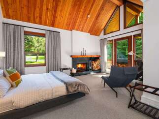 Experience ultimate relaxation in this luxurious bedroom featuring a cozy fireplace and stunning vaulted wood-paneled ceilings.