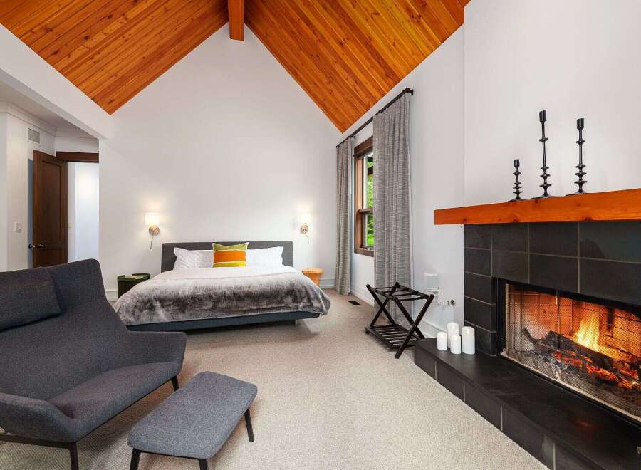 Experience ultimate comfort in this luxurious bedroom featuring a cozy fireplace and a vaulted wood-paneled ceiling.