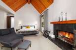 Experience ultimate comfort in this luxurious bedroom featuring a cozy fireplace and a vaulted wood-paneled ceiling.