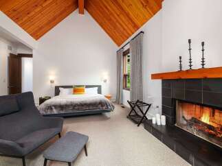 Experience ultimate comfort in this luxurious bedroom featuring a cozy fireplace and a vaulted wood-paneled ceiling.