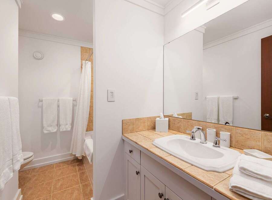 This bright and clean bathroom features a spacious vanity with a tiled countertop and a large mirror, perfect for morning routines.