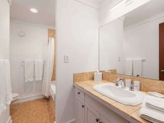 This bright and clean bathroom features a spacious vanity with a tiled countertop and a large mirror, perfect for morning routines.