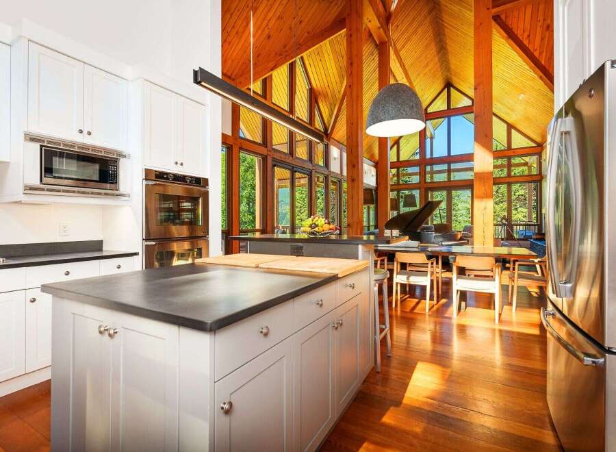 Experience luxury living in this stunning open-concept kitchen and dining area, featuring soaring vaulted ceilings with exposed wooden beams and expansive windows that flood the space with natural light.