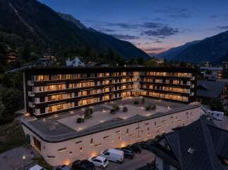 Experience luxury mountain living in this stunning property, featuring a modern hotel-style building with illuminated windows and balconies.