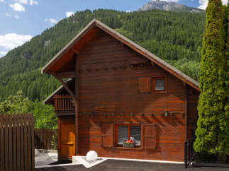 Experience the charm of this rustic wooden chalet nestled against a backdrop of lush green mountains.