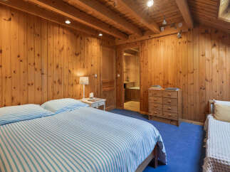 Experience cozy living in this charming wood-paneled bedroom, featuring a comfortable bed with blue and white striped linens.