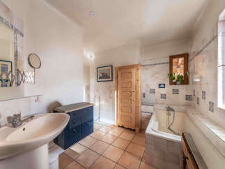 This charming bathroom features a large vanity with a pedestal sink and ample storage, complemented by a tiled bathtub and a rustic wooden cabinet.