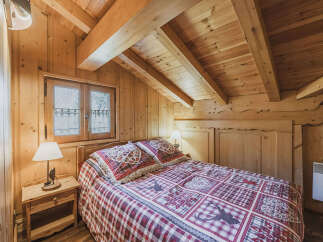 Experience rustic charm in this cozy wooden bedroom, featuring a comfortable bed adorned with charming plaid bedding and decorative pillows.