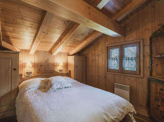 Experience rustic charm in this cozy wooden bedroom, featuring exposed beams and a comfortable bed adorned with plush linens.
