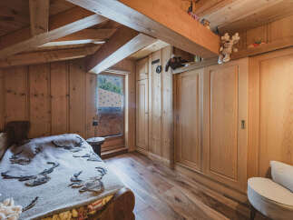 Experience rustic charm in this cozy wooden bedroom, featuring a comfortable bed adorned with a nature-themed blanket and a charming window offering scenic views.