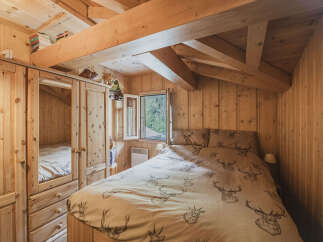 Experience rustic charm in this cozy attic bedroom, featuring warm wood paneling and exposed beams.