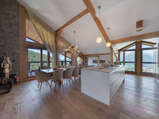 Experience luxury mountain living in this stunning open-concept dining and kitchen area, featuring vaulted ceilings with exposed wooden beams and panoramic mountain views through expansive windows.