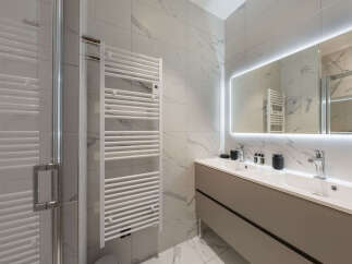 Experience modern luxury in this stunning bathroom featuring a sleek double vanity with illuminated mirror and elegant marble-look tiles.