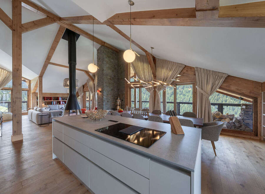Experience luxury mountain living in this stunning open-plan chalet, featuring a modern kitchen island with a built-in cooktop, a suspended fireplace, and a spacious dining area.