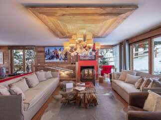 Experience luxurious mountain living in this stunning chalet, featuring a grand living room with a rustic wooden ceiling and a striking chandelier.