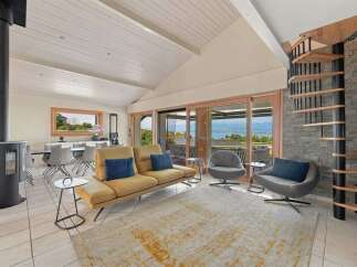Experience breathtaking lake views from this stunning living area, featuring a modern yellow sofa and comfortable grey armchairs.