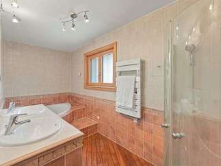 This elegant bathroom features a double vanity with modern faucets, a luxurious corner bathtub, and a spacious glass-enclosed shower.