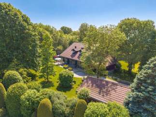 Nestled amidst lush greenery, this charming property features a main house with a classic tiled roof and an inviting outdoor patio area perfect for relaxation.