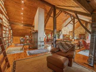 Discover this stunning rustic living space featuring soaring wooden beamed ceilings and an expansive floor-to-ceiling bookshelf, perfect for the avid reader.