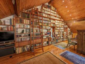 Immerse yourself in this stunning library, featuring floor-to-ceiling bookshelves that reach the vaulted wooden ceiling.