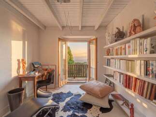 This charming room features a cozy reading nook with a desk and chair, bathed in warm sunlight streaming through double doors.