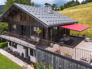 Experience alpine charm in this rustic wooden chalet, featuring a spacious wooden deck with a red awning perfect for outdoor dining and relaxation.
