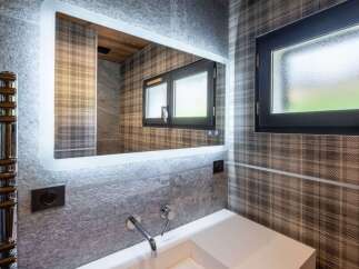 Experience modern luxury in this stylish bathroom, featuring a sleek vanity with a contemporary faucet and a large, illuminated mirror.