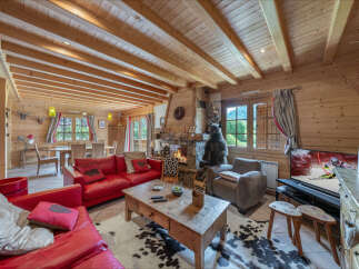 Experience cozy living in this charming log cabin living room, featuring a roaring fireplace and plush red sofas perfect for relaxing.