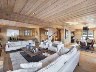 Experience luxurious alpine living in this stunning wooden chalet, featuring a spacious open-plan living area with plush white sofas and a modern coffee table.