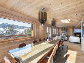 Experience luxurious mountain living in this stunning chalet, featuring a spacious dining area with a long, polished wooden table and comfortable leather chairs.