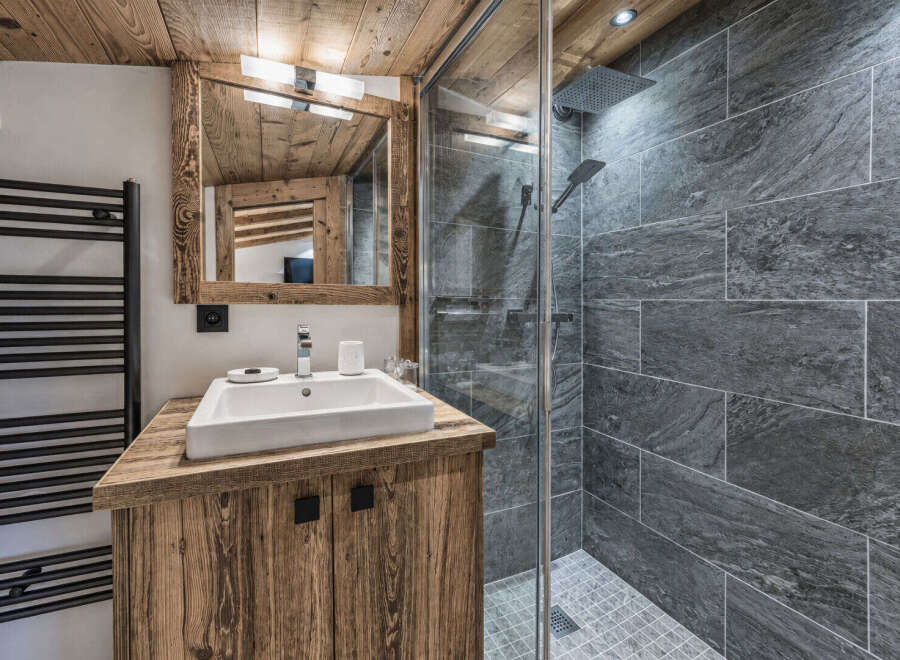 Experience rustic charm in this mountain-style bathroom, featuring a wooden vanity with a modern white sink and a sleek glass-enclosed shower with stone tile accents.