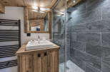 Experience rustic charm in this mountain-style bathroom, featuring a wooden vanity with a modern white sink and a sleek glass-enclosed shower with stone tile accents.