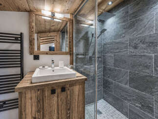 Experience rustic charm in this mountain-style bathroom, featuring a wooden vanity with a modern white sink and a sleek glass-enclosed shower with stone tile accents.