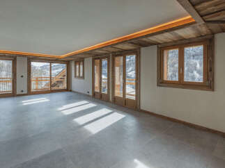 Experience luxurious mountain living in this spacious, open-plan room featuring large windows and sliding glass doors that offer breathtaking views of the snowy landscape.