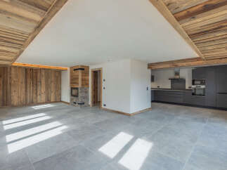Experience modern alpine living in this stunning open-plan space, featuring a rustic wood-paneled wall and a striking stone fireplace.