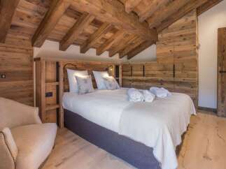 Experience rustic charm in this cozy bedroom, featuring exposed wooden beams and a luxurious bed adorned with plush towels and robes.