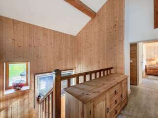 Experience rustic charm in this beautifully appointed wooden interior, featuring a charming staircase with a wooden railing and a quaint window overlooking a green landscape.