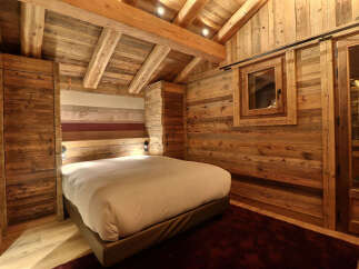 Experience rustic luxury in this charming chalet bedroom, featuring a cozy bed with a stylish headboard and warm wooden accents throughout.