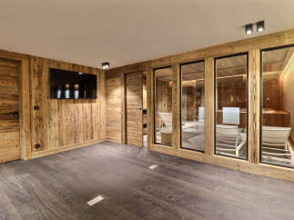 Experience ultimate relaxation in this luxurious wooden-paneled room, featuring a sleek flat-screen TV and a spa-like area with lounge chairs visible through glass doors.