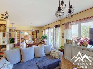 This charming living and dining area features a comfortable sofa, a large wooden dining table, and ample natural light streaming in from the patio doors.