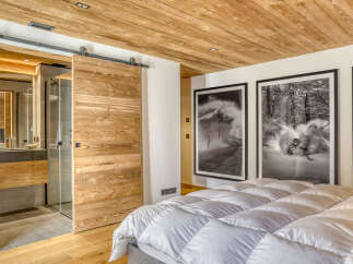 Experience luxury mountain living in this stunning bedroom featuring a rustic wooden barn door that slides open to reveal a modern en-suite bathroom.